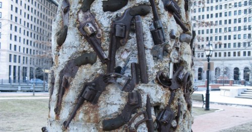 A close-up of the Gun Totem sculpture in Providence, showing decommissioned firearms encased in a concrete pillar.