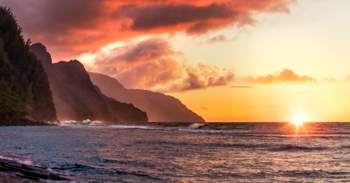 A fiery sunset against the rugged mountains of a Hawaiian Island coast.