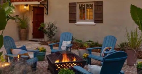 Backyard of Spanish-inspired Airbnb in Minden, Louisiana. Four blue chairs, a fire pit, and an adobe-style exterior on the home in the background