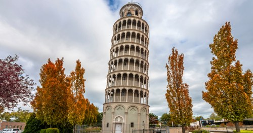 An Italian-style tower leans between fall trees.
