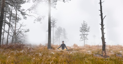 A woman sits on frozen ground and meditates while winter fog looms overhead.