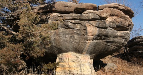 A large, mushroom-shaped rock formation with a thick cap and narrow base at Mushroom Rock State Park in Kansas.