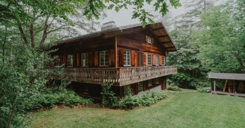 A side exterior view of The Chalet, a Swiss-inspired Airbnb property in Nelson, NH. The alpine-style home is surrounded by green trees and shrubbery.
