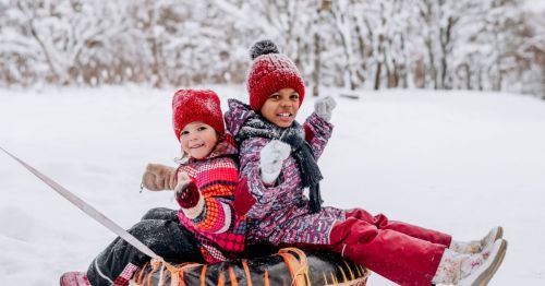 A beautiful, smiling kids with knit hats, happily smiling, while sitting on an orange and black snow tube.