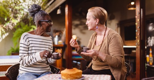 Two retired women enjoy coffee and conversation on a sunny outdoor patio in a Pennsylvania senior community.
