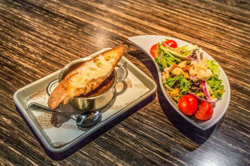 Close up of a metal bowl of Bourbon French Onion soup topped with a cheesy crostini.