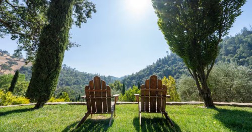 Two wooden chairs sit on a grassy lawn, overlooking a lush green valley.
