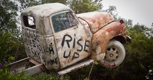 A rusty, graffiti-covered vintage truck body angled upward toward the trees at Truckhenge in Topeka, Kansas.