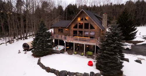 The exterior of a two-story Swiss-style chalet surrounded with snow and trees.