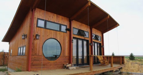The exterior of a small cabin Airbnb in Powell, Wyoming, with a wooden deck, clean lines, and large windows.