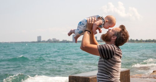 A man holding a small baby with the water in the background at Promontory Point Chicago, Illinois
