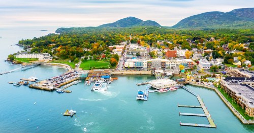 An aerial view captures the busy harbor, piers, and lush coastal landscape of Bar Harbor, Maine.