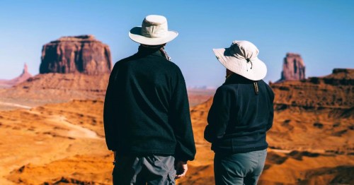 A couple in dark clothing standing in front of unique rock formations in a vast desert landscape in Utah.