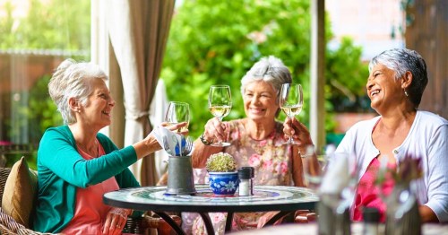 Three happy retired women enjoying drinks together at a table in a cheerful outdoor setting in Texas.