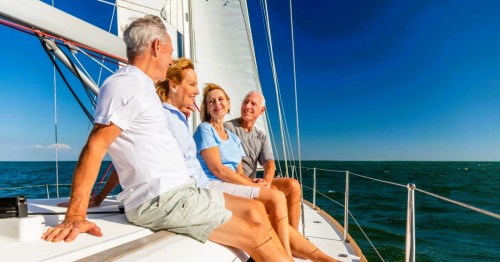 Four elderly adults enjoying a sunny day sailing on a boat in Rhode Island, with a clear blue sky and ocean in the background.