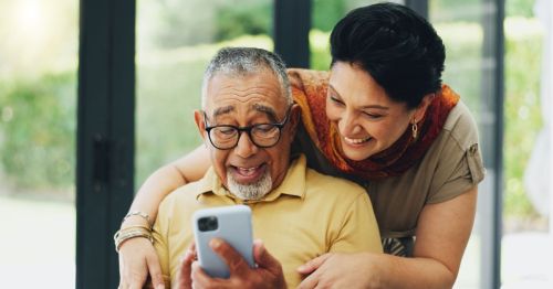 A happy retired couple in New Mexico, laughing while looking at something on a cell phone.