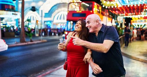 A happy couple is walking along the Las Vegas strip surrounded by dazzling lights.