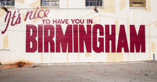 A red mural on the side of a cream building that reads It's Nice to Have You In Birmingham.