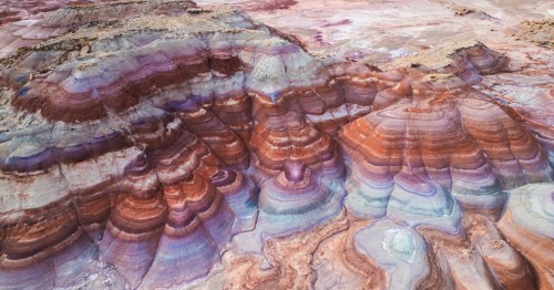 Colorful mounds of Utah's Bentonite Hills display striking layers of purple, blue, red, and gray clay, forming rounded, otherworldly shapes across the desert.