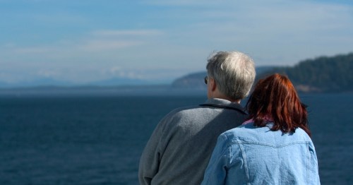A retired couple watching the Alaskan Ocean with their backs to the camera.