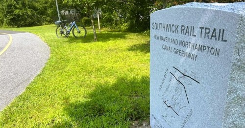 Grannite sign marking the Southwick Rail Trail in MA, set against a grassy area and a bike parked nearby.