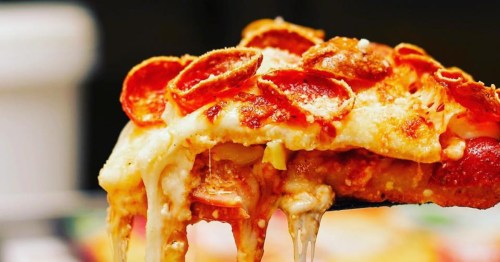 A close-up of a thick pizza slice with melting cheese and crispy curled pepperoni being lifted.