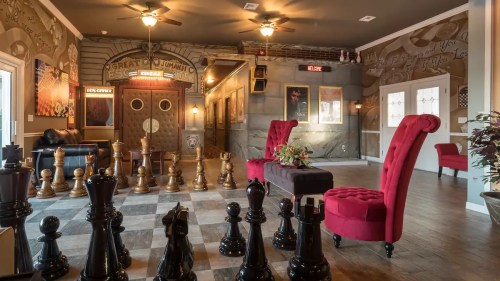 A stylish room featuring large chess pieces, red chairs, and decorative walls with vintage-style decor.