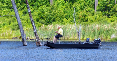 an elderly man sits with a fishing pole on a boat on a lake in arkansas
