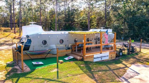 A unique helicopter-shaped structure with a deck, surrounded by trees and grass, featuring an American flag.