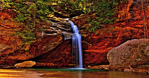 A majestic waterfall flows over orange rocks, a perfect sight for a family hiking in Ohio.