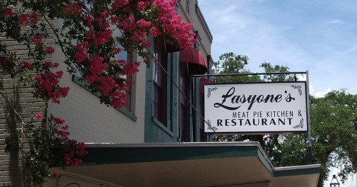 sign for lasyone's meat pie kitchen on a building covered in pink roses in louisiana