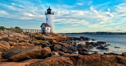 A small white lighthouse sits on a sprawling group of rocks before an ocean cove.
