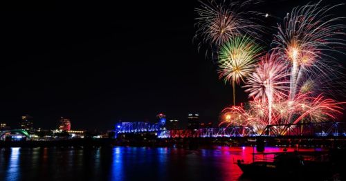 Colorful fireworks over the skyline of Little Rock Arkansas, with an illuminated bridge and city lights glowing on the river.