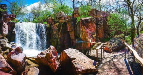 Winnewissa Falls cascades over vivid pink quartzite rocks beside a paved trail at Pipestone National Monument in MN.