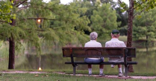 two elderly men sit on a park bencg overlooking a lake in oklahoma