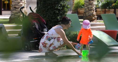 a mom crouches by her toddler playing in the water at a splash pad in scottsdale az