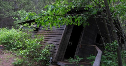The slanted entrance of the Montana Vortex and House of Mystery, partially hidden by trees and foliage, with the doorway visibly skewed to enhance the disorienting effect.