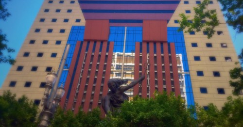 Portlandia statue in front of the Portland Building in downtown Portland, Oregon, with the postmodern facade reflected in blue glass windows, highlighting why it’s often listed among the strangest buildings in Oregon.