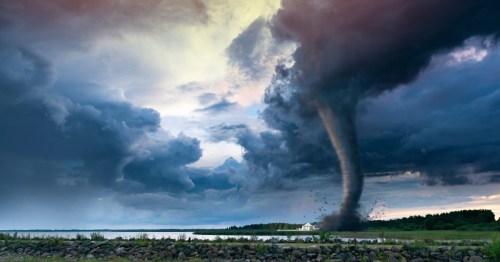 a dramatic shot of a dark sky and a tornado over green landscape and a body of water in the midwest