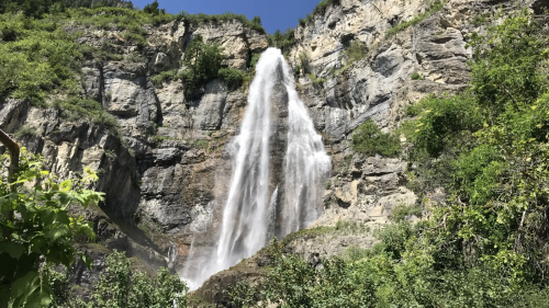 A majestic waterfall cascading down rocky cliffs, surrounded by lush greenery and a clear blue sky.