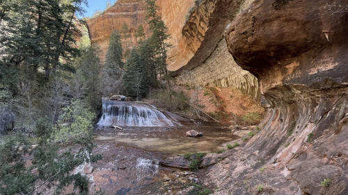 A serene landscape featuring a waterfall, rocky cliffs, and lush greenery in a canyon setting.