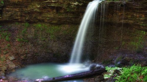 A serene waterfall cascades into a tranquil pool, surrounded by lush greenery and rocky cliffs.