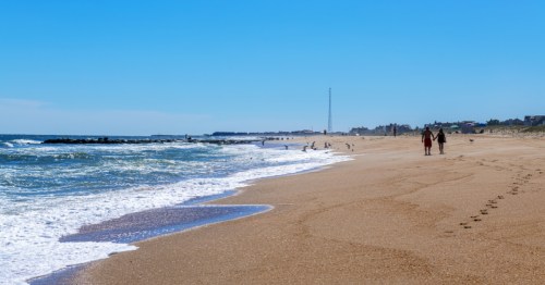 A panoramic shot of a New Jersey beach, with two people in the background walking on the sand.