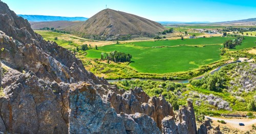 An aerial view of a rocky mountain side, green valley, and the town of Cokeville, Wyoming, in the distance.