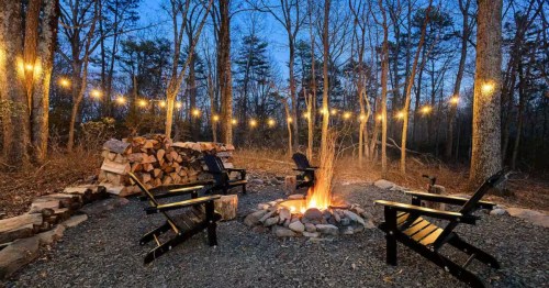 An outdoor fire pit with lawn chairs and string lights at sunset.