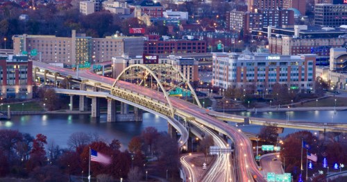 Aerial view of the yellow Fort Pitt Bridge crossing the Monongahela River toward the downtown Pittsburgh skyline.