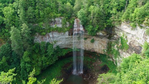 A stunning waterfall cascades down a rocky cliff, surrounded by lush green trees and vegetation.