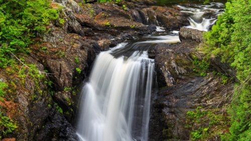 A serene waterfall cascading over rocky terrain, surrounded by lush green foliage.