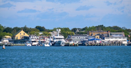 A wide scenic view of the Greenport waterfront, featuring docked boats and the village skyline.