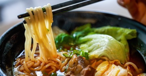 A close-up of a bowl of ramen with two chopsticks holding up strands of noodles.